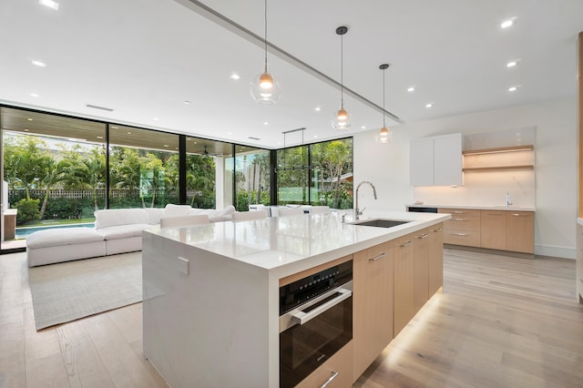 kitchen featuring hanging light fixtures, an island with sink, stainless steel oven, light brown cabinets, and sink