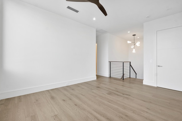 spare room featuring ceiling fan with notable chandelier and light hardwood / wood-style flooring