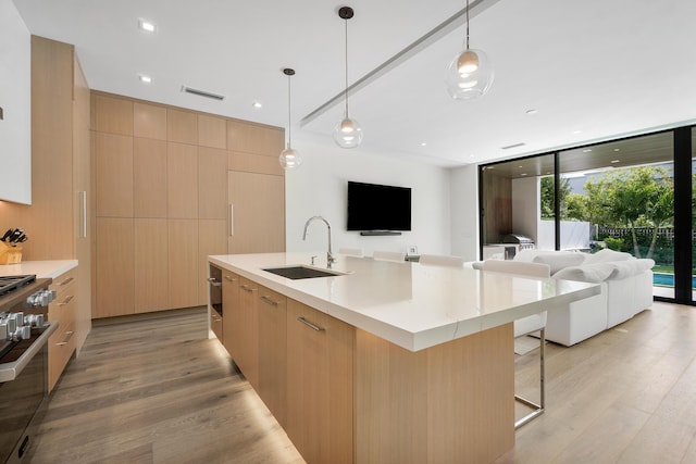 kitchen with sink, light brown cabinets, a large island with sink, and pendant lighting