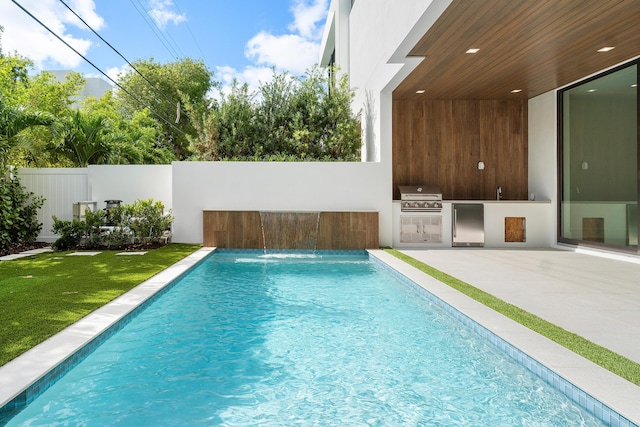 view of swimming pool featuring a lawn, pool water feature, an outdoor kitchen, a patio area, and area for grilling