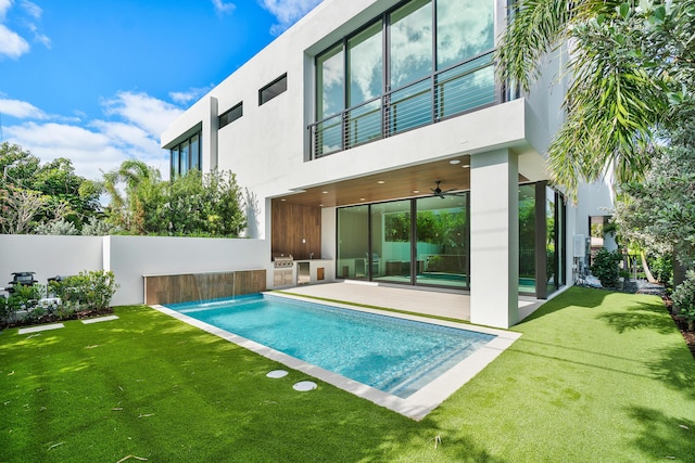 rear view of property featuring a balcony, a lawn, a patio area, exterior kitchen, and pool water feature