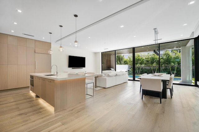 kitchen featuring sink, decorative light fixtures, a wall of windows, a large island, and light brown cabinetry