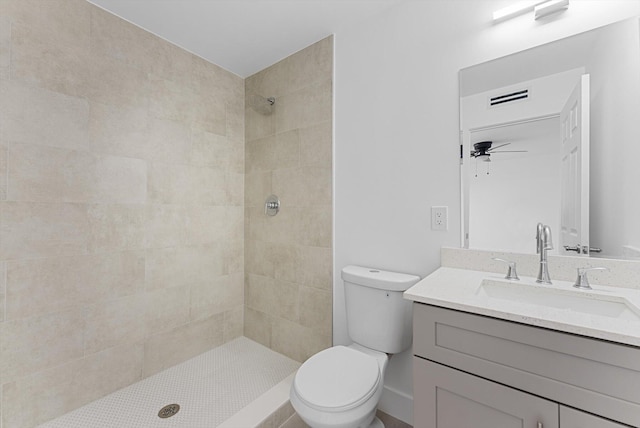 bathroom with ceiling fan, vanity, toilet, and a tile shower