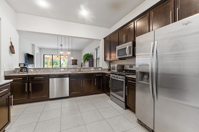 kitchen with a sink, light stone counters, stainless steel appliances, light tile patterned flooring, and dark brown cabinets