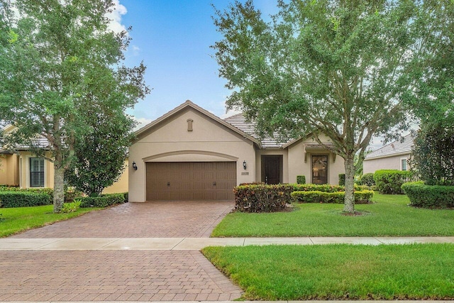 ranch-style home with stucco siding, decorative driveway, a front yard, and an attached garage