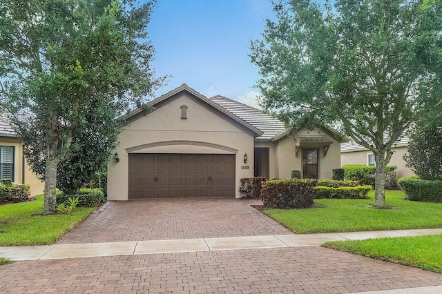 ranch-style house featuring a tile roof, a front yard, stucco siding, decorative driveway, and an attached garage