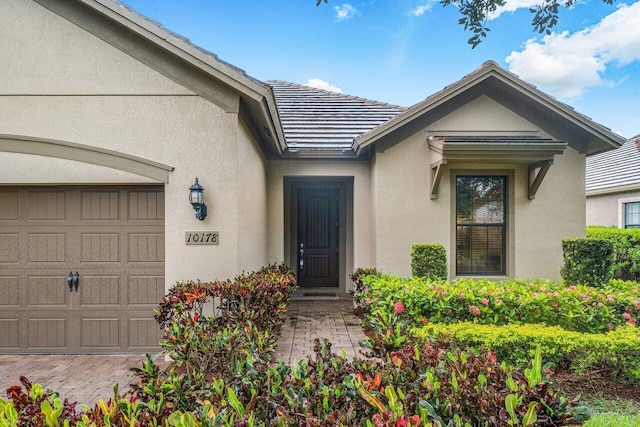 view of exterior entry with stucco siding, an attached garage, and a tiled roof