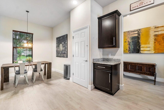 kitchen with baseboards, dark brown cabinetry, pendant lighting, light stone counters, and light wood-style floors