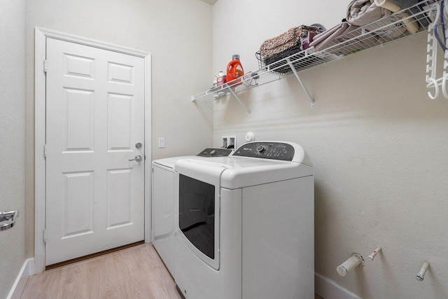 clothes washing area featuring laundry area, separate washer and dryer, light wood-type flooring, and baseboards