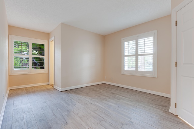 empty room with plenty of natural light, a textured ceiling, and light hardwood / wood-style flooring