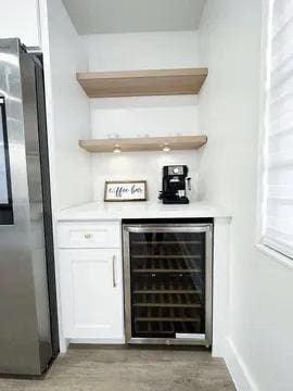 bar featuring white cabinets, dark hardwood / wood-style flooring, wine cooler, and stainless steel refrigerator