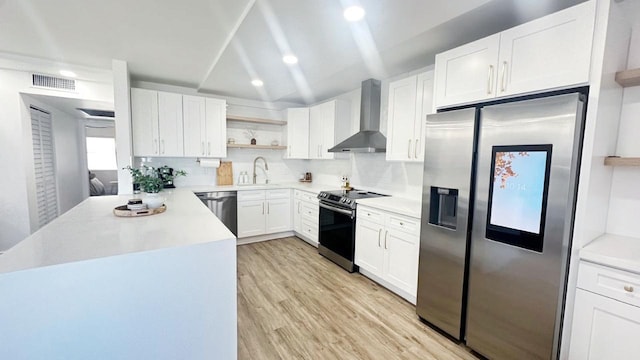 kitchen with wall chimney exhaust hood, backsplash, appliances with stainless steel finishes, white cabinets, and light wood-type flooring