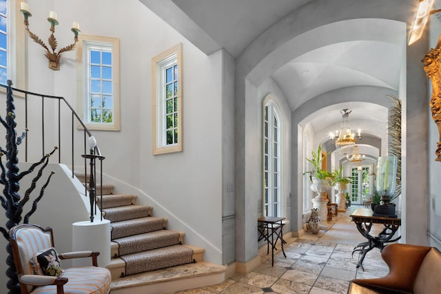 entrance foyer featuring stone tile floors, stairway, arched walkways, an inviting chandelier, and baseboards