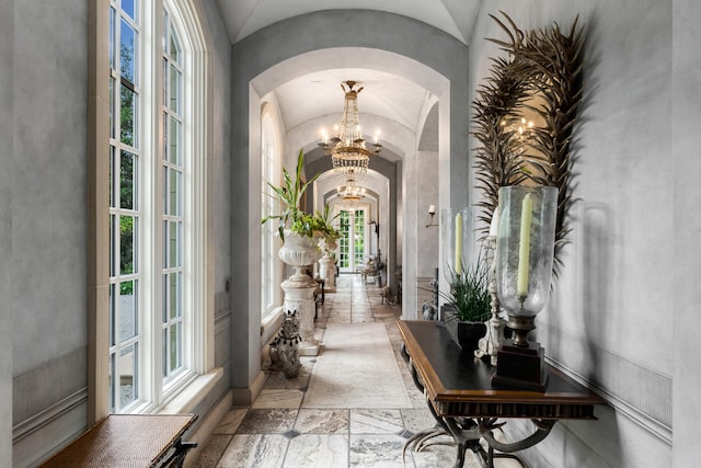 corridor with a wealth of natural light, an inviting chandelier, tile floors, and lofted ceiling