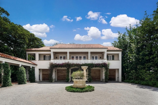 mediterranean / spanish-style home featuring stucco siding, driveway, a tile roof, an attached garage, and a balcony