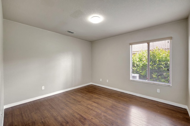 spare room featuring visible vents, a textured ceiling, baseboards, and dark wood-style flooring