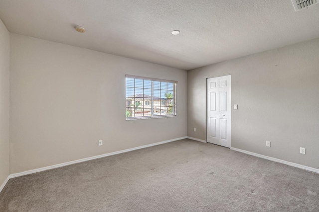 empty room with visible vents, light colored carpet, a textured ceiling, and baseboards