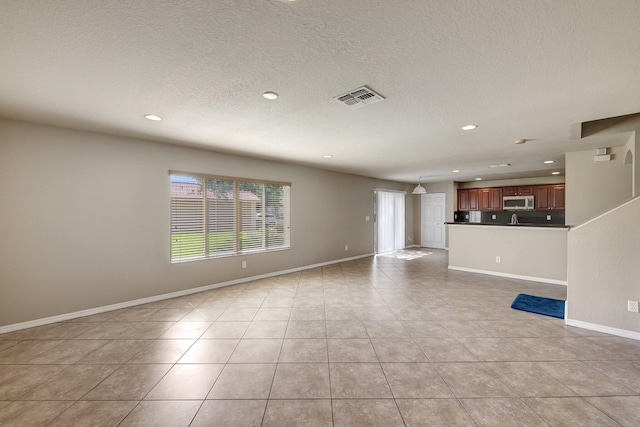 unfurnished living room with light tile patterned floors, visible vents, a textured ceiling, and baseboards