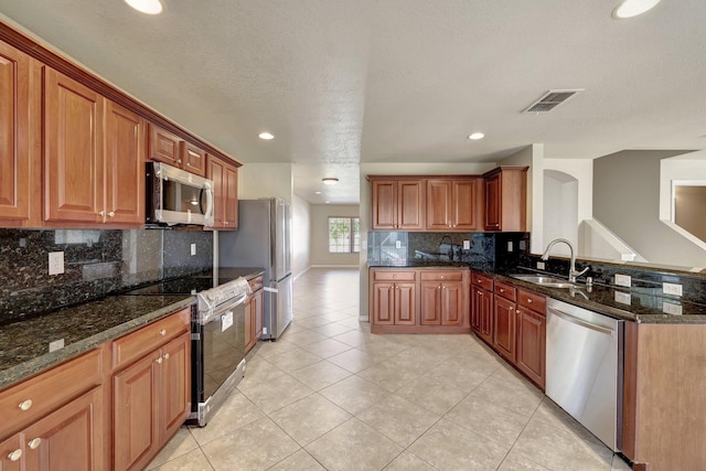 kitchen featuring visible vents, backsplash, dark stone counters, appliances with stainless steel finishes, and a sink