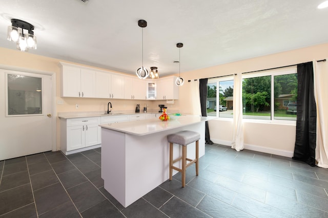 kitchen featuring a breakfast bar, white cabinets, dark tile patterned flooring, sink, and hanging light fixtures