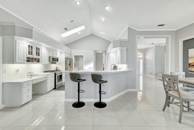 kitchen with light tile patterned flooring, a breakfast bar, kitchen peninsula, stainless steel appliances, and white cabinets