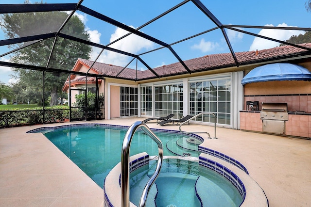 view of swimming pool featuring area for grilling, a pool with connected hot tub, a patio area, glass enclosure, and an outdoor kitchen