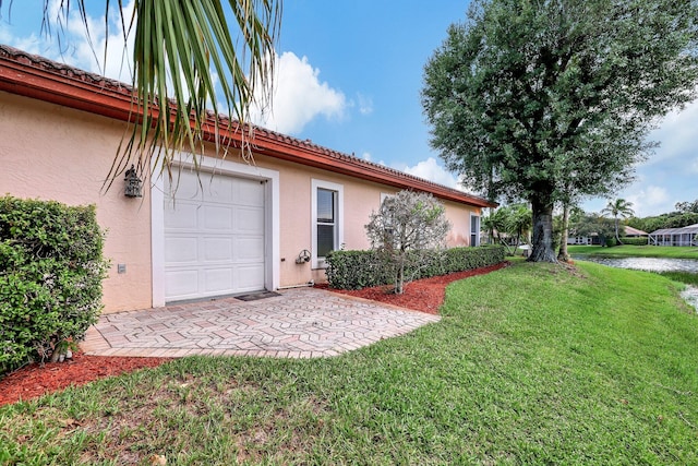 view of property exterior with a lawn, a tiled roof, a garage, and stucco siding