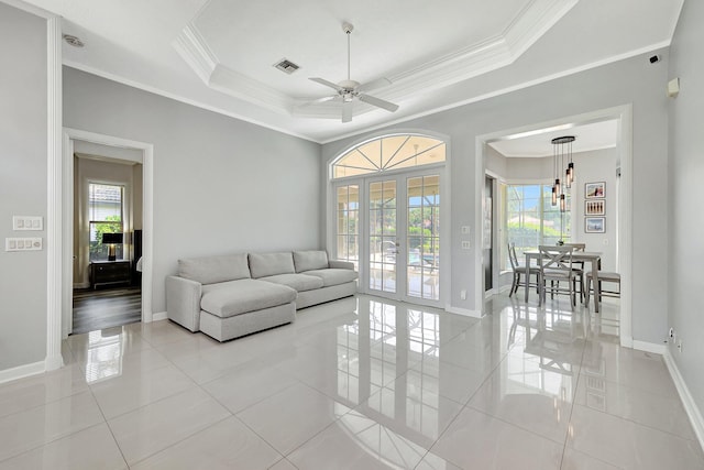 tiled living room with crown molding, a healthy amount of sunlight, a raised ceiling, and french doors