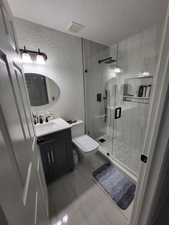 bathroom with vanity, toilet, a shower with shower door, and a textured ceiling