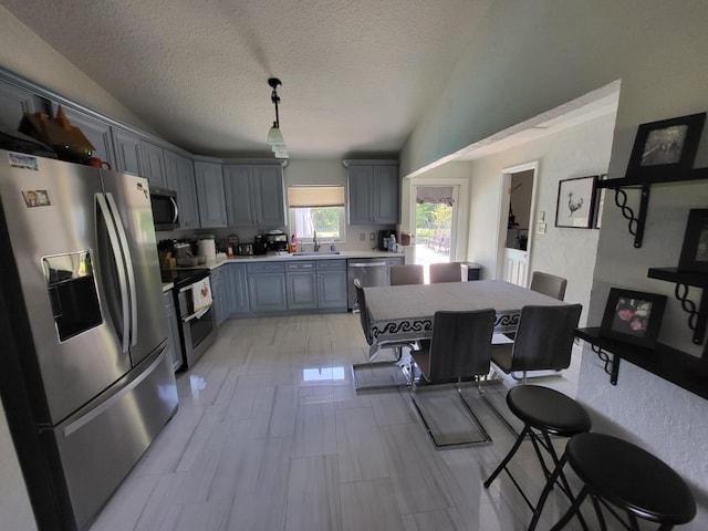 kitchen with pendant lighting, sink, a textured ceiling, a kitchen island, and stainless steel appliances