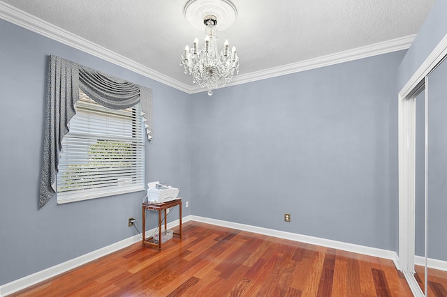 spare room with hardwood / wood-style floors, a textured ceiling, crown molding, and a notable chandelier