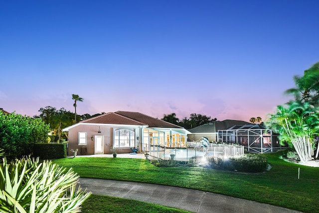 back house at dusk with a lawn and glass enclosure