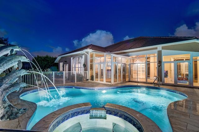 pool at dusk with pool water feature, a patio, and an in ground hot tub