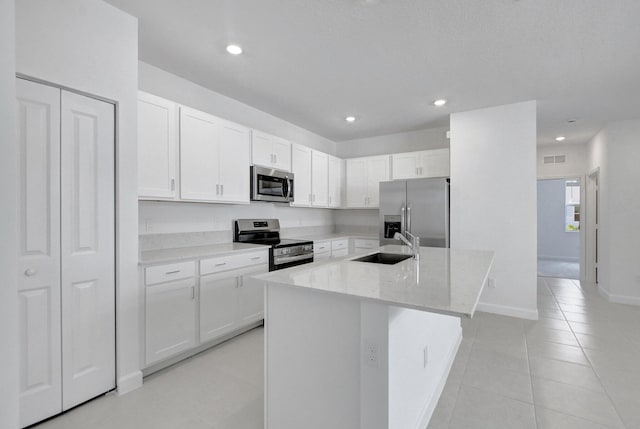 kitchen with light stone countertops, appliances with stainless steel finishes, sink, white cabinets, and an island with sink