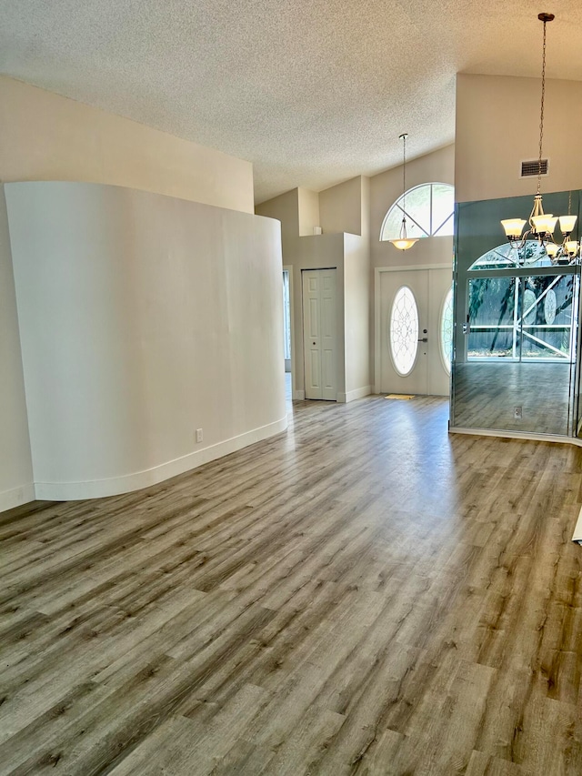 unfurnished living room with wood-type flooring, high vaulted ceiling, a chandelier, and a textured ceiling