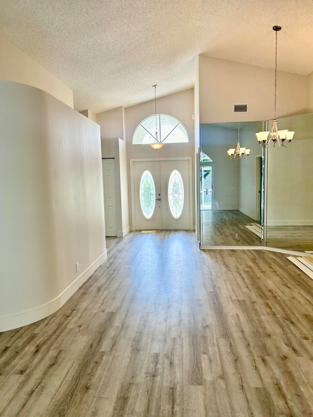 entryway featuring a notable chandelier, a textured ceiling, hardwood / wood-style flooring, and high vaulted ceiling