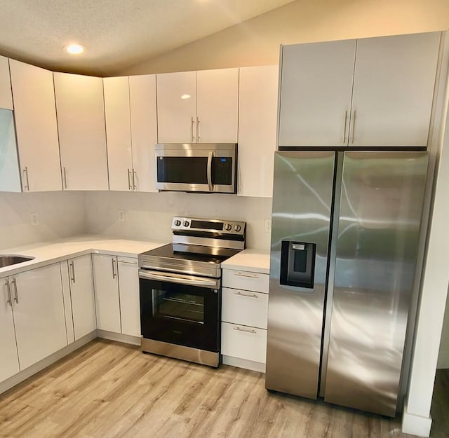 kitchen featuring white cabinets, light hardwood / wood-style floors, vaulted ceiling, and appliances with stainless steel finishes