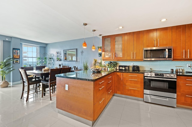 kitchen featuring hanging light fixtures, tasteful backsplash, dark stone countertops, light tile patterned flooring, and appliances with stainless steel finishes