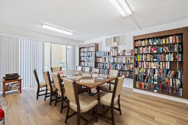 dining space featuring an AC wall unit, light hardwood / wood-style flooring, and a textured ceiling