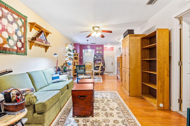 living room featuring a textured ceiling, light wood-type flooring, and ceiling fan