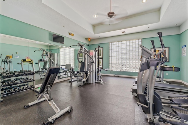 exercise room featuring ceiling fan, a raised ceiling, and a textured ceiling