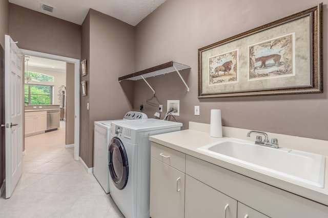 clothes washing area featuring sink, washer and dryer, cabinets, and light tile patterned floors