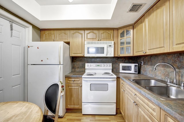 kitchen with tasteful backsplash, white appliances, light wood-type flooring, a raised ceiling, and sink