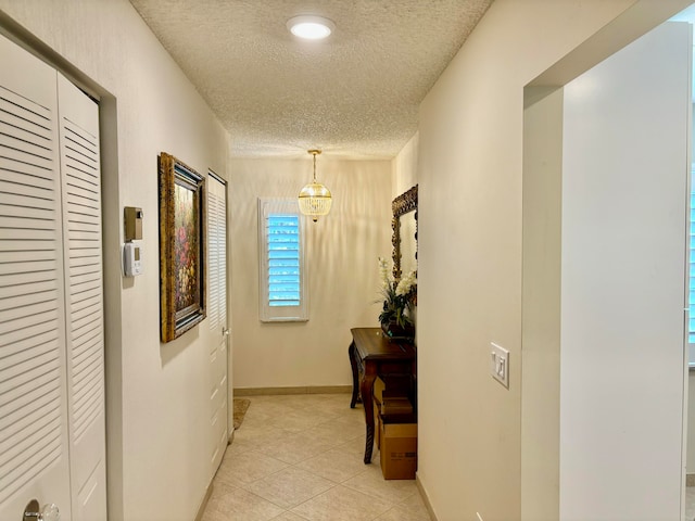 hallway with light tile patterned flooring, a textured ceiling, and a notable chandelier