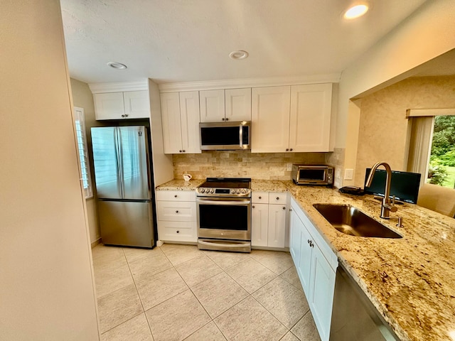 kitchen with light stone counters, stainless steel appliances, sink, white cabinetry, and light tile patterned flooring