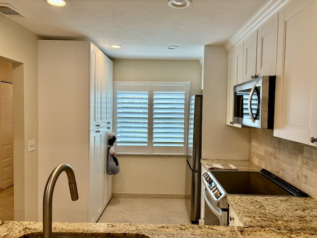 kitchen featuring white cabinets, stainless steel appliances, light stone counters, and decorative backsplash