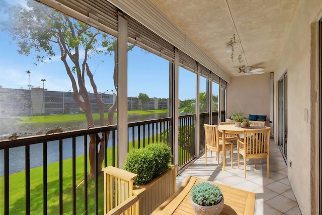 sunroom with ceiling fan and a water view