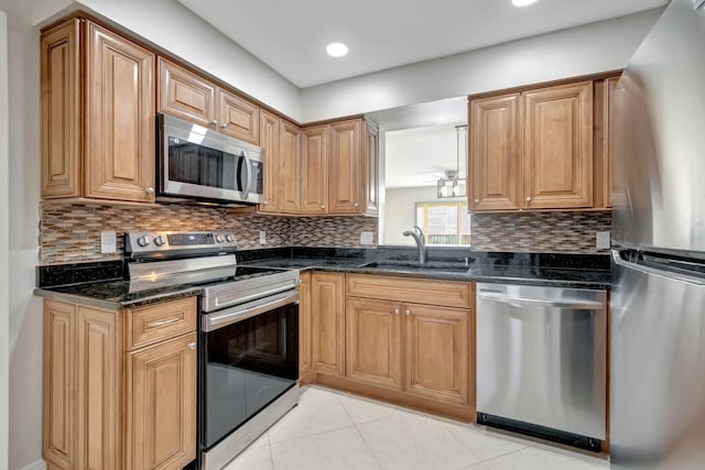 kitchen with light tile patterned floors, appliances with stainless steel finishes, backsplash, dark stone countertops, and sink