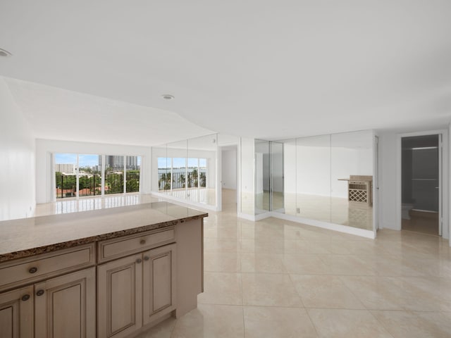 kitchen featuring light tile patterned floors, open floor plan, brown cabinets, and light stone countertops