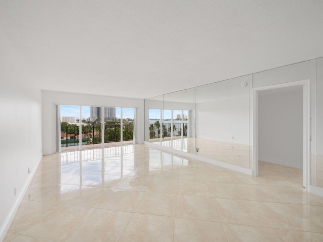 empty room featuring a textured ceiling, light tile patterned flooring, and baseboards